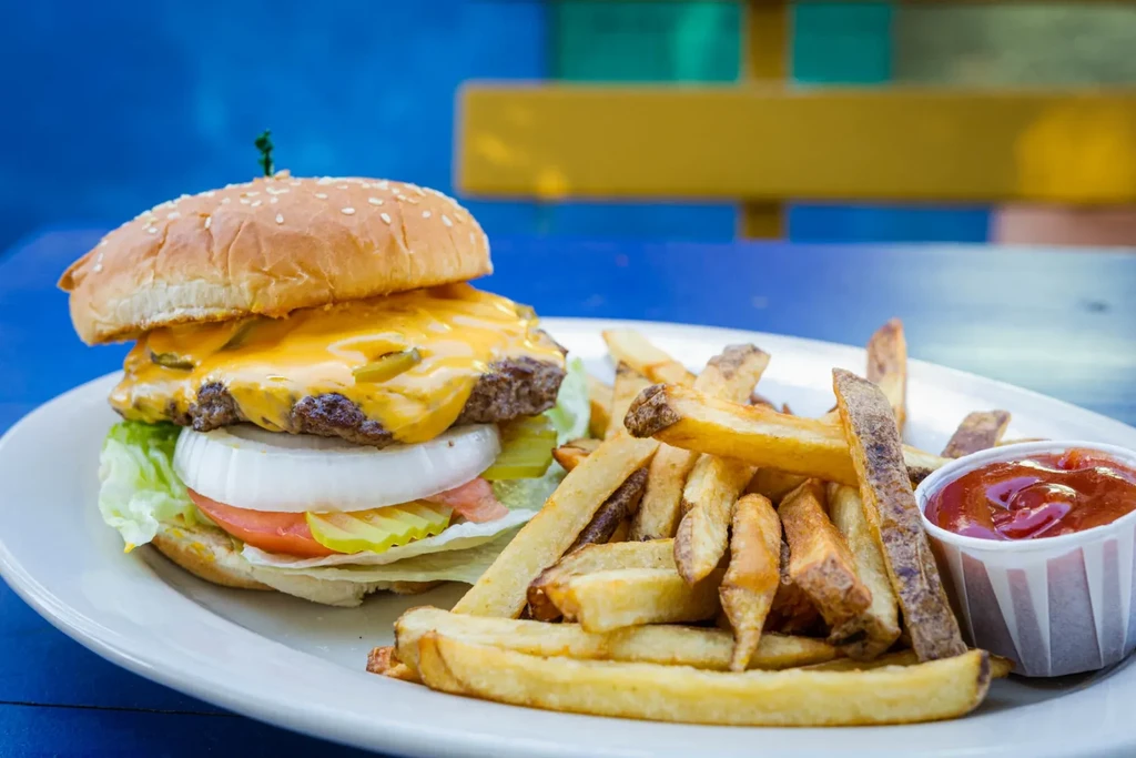 Close-up cheeseburger with jalapeños, fries, and ketchup on a white plate.