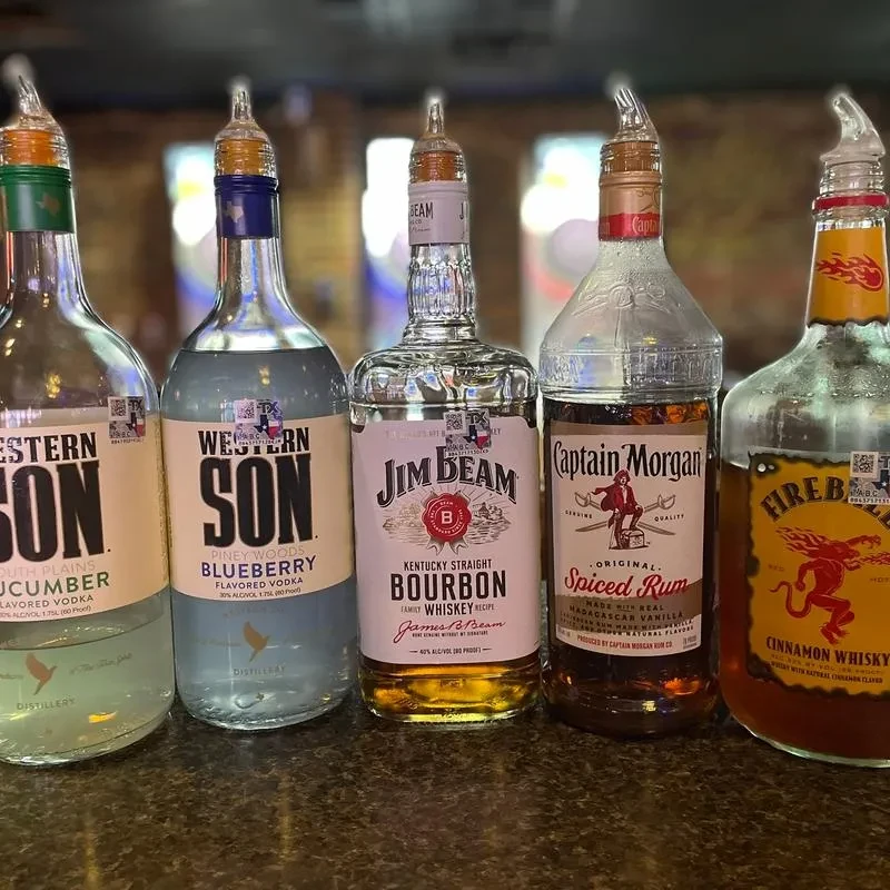 Five assorted liquor bottles with pour spouts on a bar.