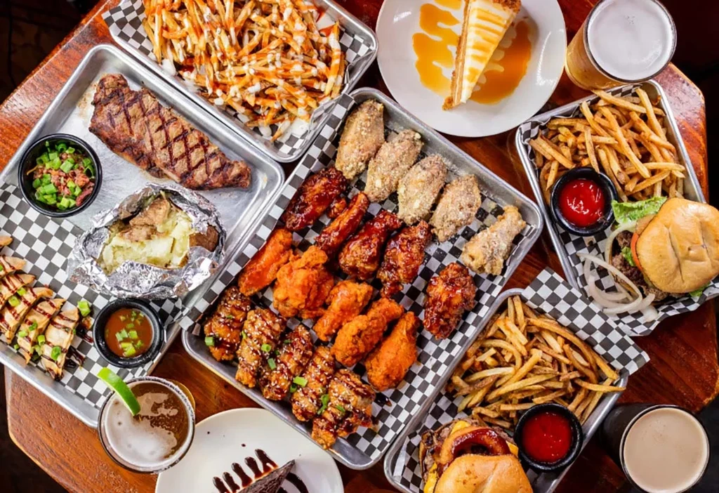 Varied food spread: steak, wings, burgers, fries, desserts, and drinks.