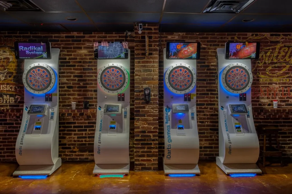 Four white electronic dartboards glowing in a dimly lit bar.