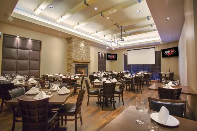 Empty, upscale restaurant with set tables, a burning fireplace, and screens.