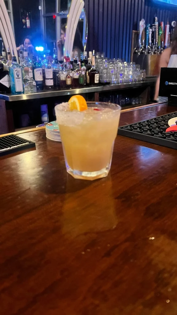 Amber cocktail with orange slice and sugared rim on wooden bar.