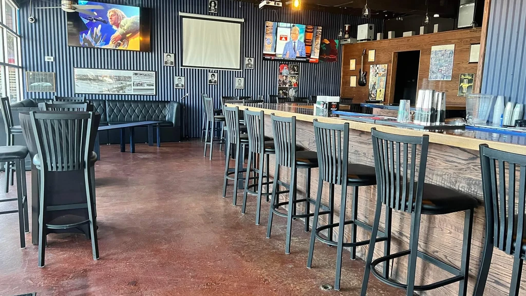 Empty modern bar interior with bar stools, booths, and multiple TV screens.