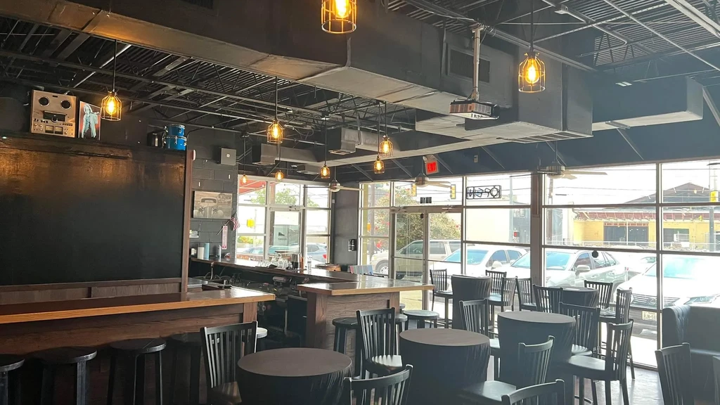Empty modern industrial restaurant with bar, high-top tables, and large windows.