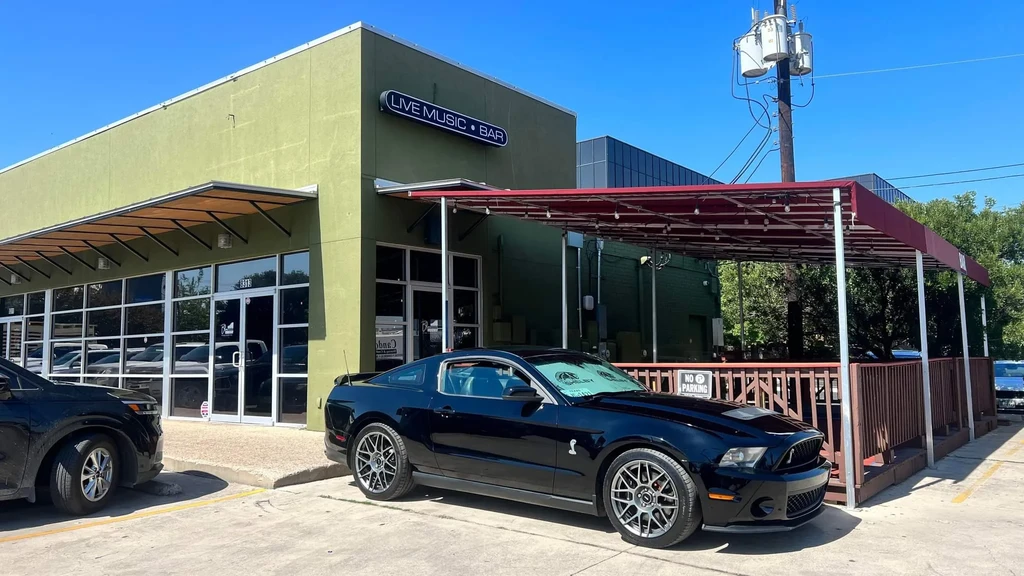 Olive green bar with "LIVE MUSIC" sign, black Mustang parked outside.