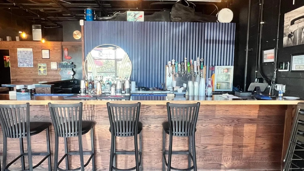 Bar interior with wooden counter, five stools, taps, and industrial decor.