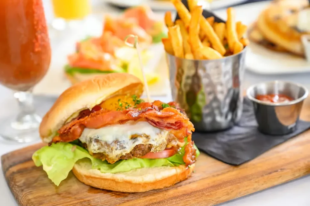 Gourmet burger with bacon, fried egg, cheese, lettuce, tomato, and fries.