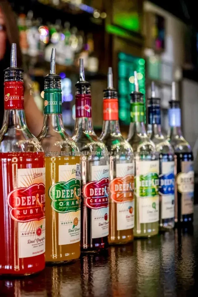 Eight Deep Eddy flavored spirits with spouts on a bar counter.