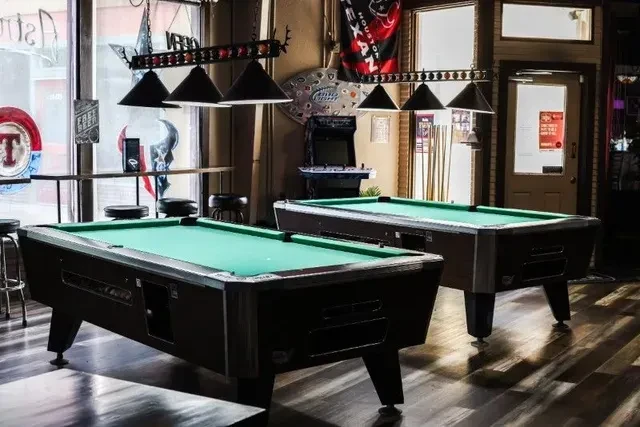 Brightly lit bar interior with two green felt pool tables.