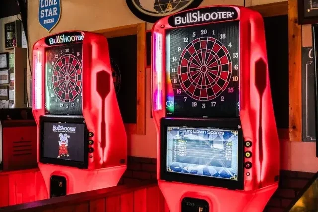 Two BullShooter electronic dart machines glow red in a dark bar.