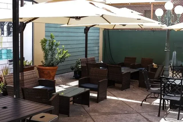 Empty outdoor restaurant patio with brown wicker tables, chairs, and umbrellas.