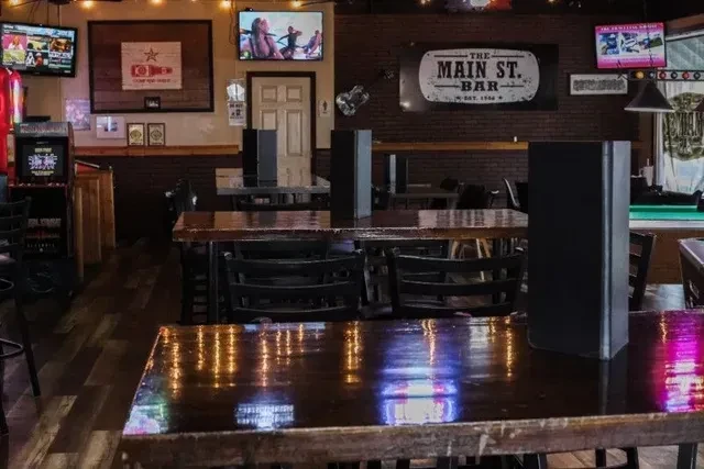 Dimly lit Main St. Bar: empty tables, TVs, arcade, pool table.
