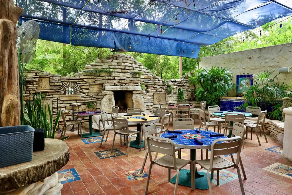Outdoor restaurant patio with rustic stone, mosaic tables, and string lights.
