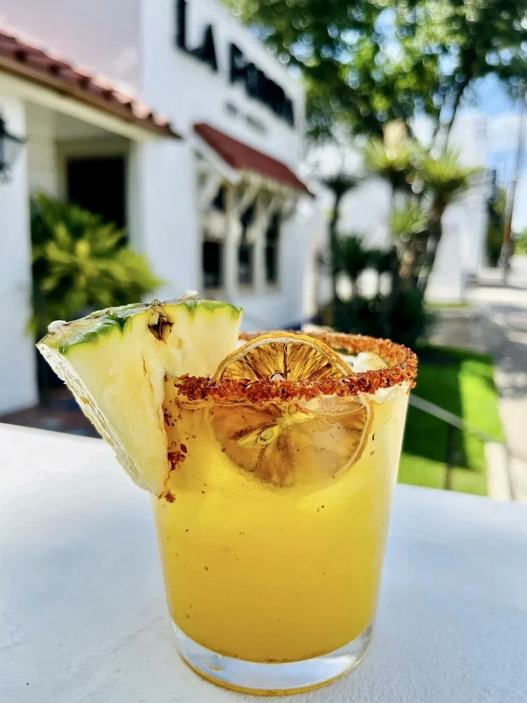 Yellow-orange drink with pineapple, dried citrus, and spiced rim, outdoors.