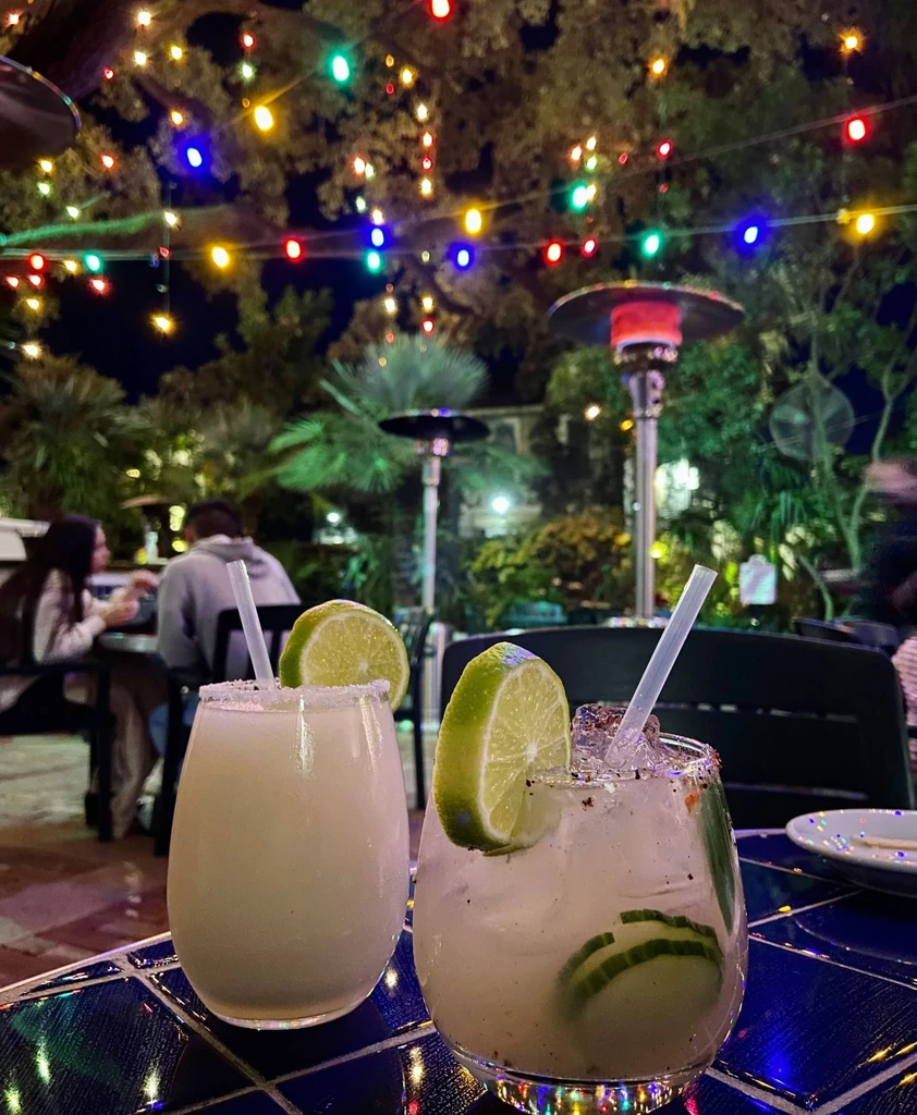 Cocktails on blue tiled table, outdoor evening bar with string lights.