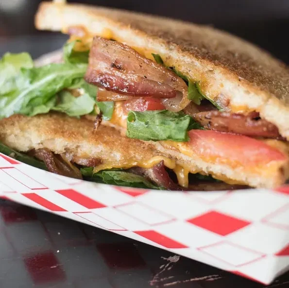 Grilled sandwich halves with cheese, bacon, lettuce, tomato in a tray.
