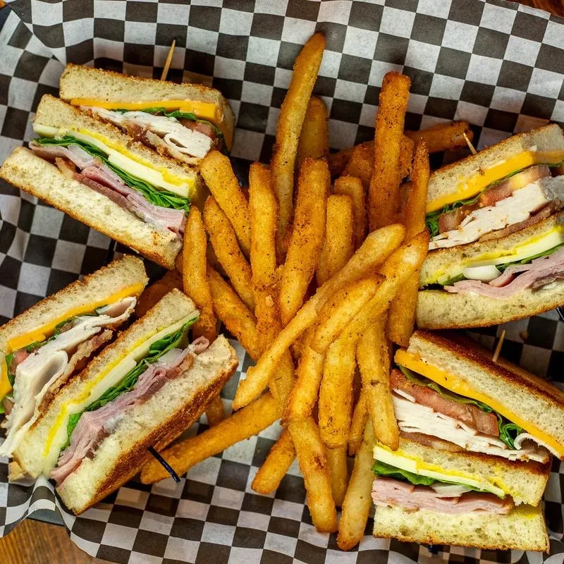 Overhead view of club sandwiches and fries in a checkered basket.