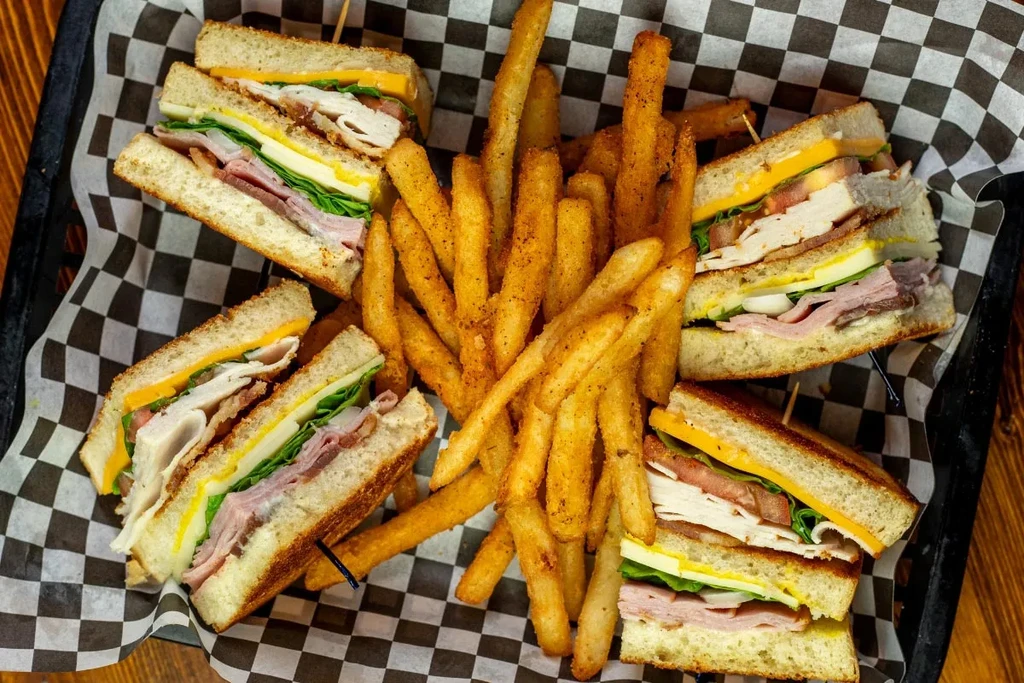 Diagonally cut club sandwiches and seasoned fries in a checkered basket.