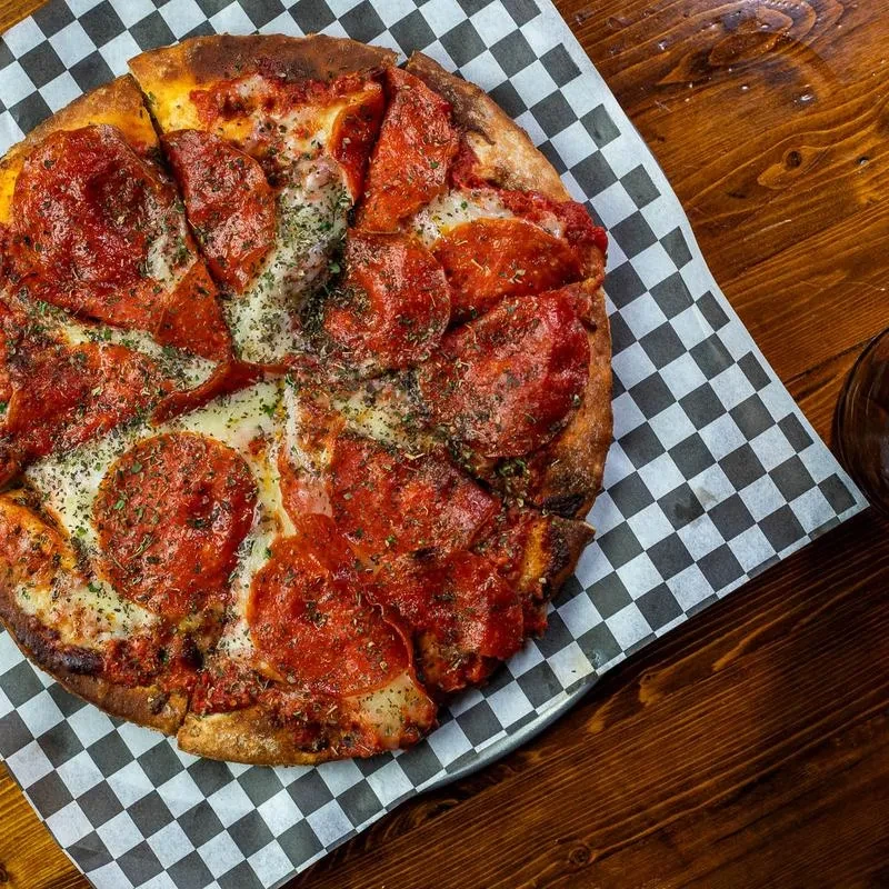 Freshly baked pepperoni pizza, sliced and garnished with green herbs.