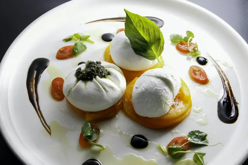 Plated burrata cheese with tomatoes, pesto, basil, and balsamic glaze.