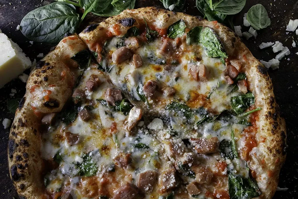 Close-up pizza with charred crust, white cheese, spinach, and sausage.