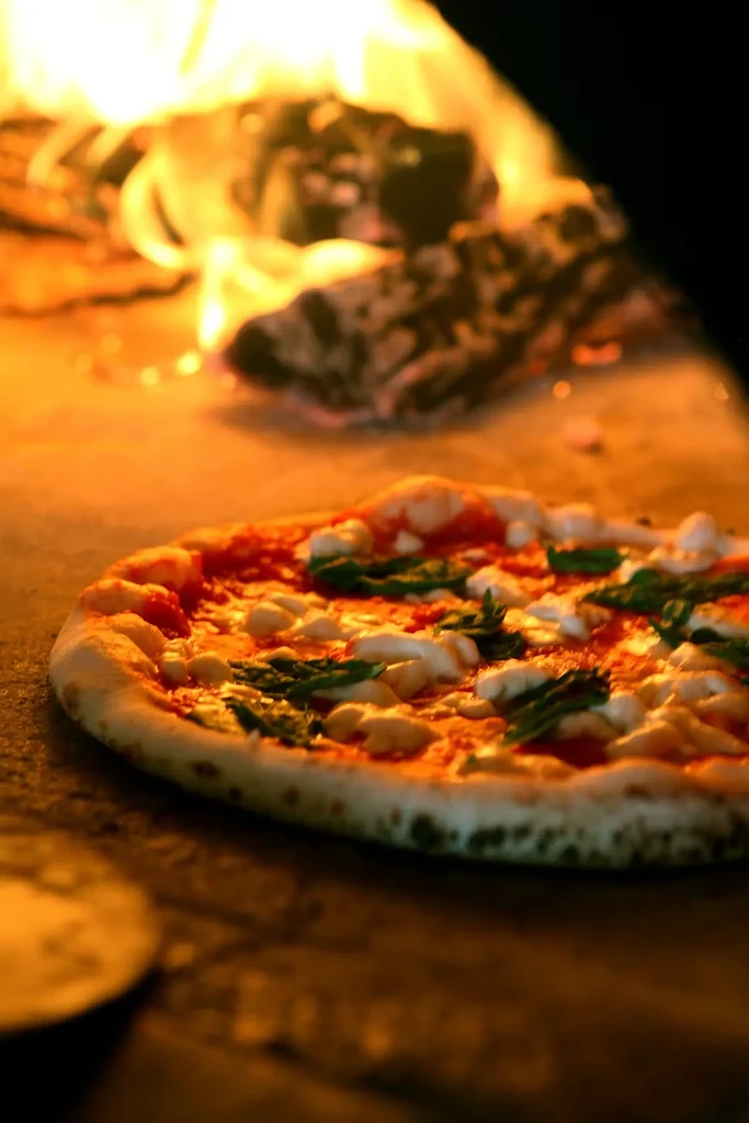 Fresh Neapolitan pizza baking in a wood-fired oven with glowing flames.