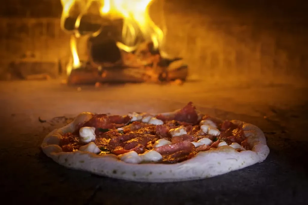 Partially baked pepperoni pizza cooking in a glowing wood-fired oven.