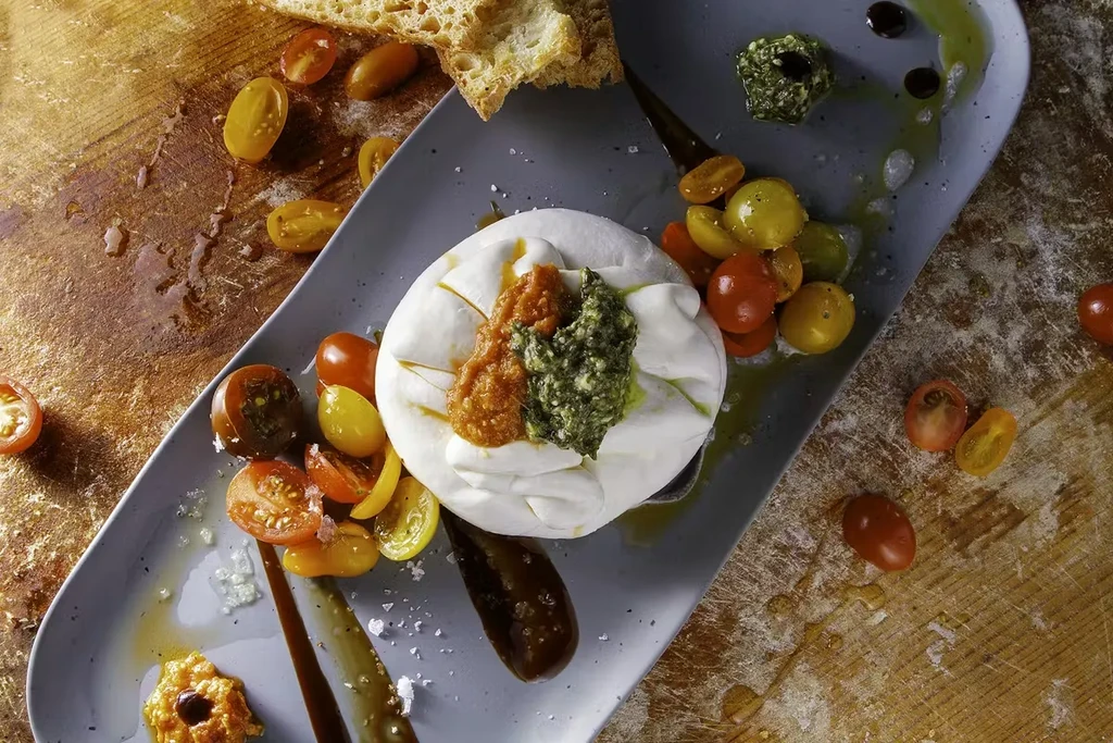 Creamy cheese, pesto, tomatoes, balsamic on grey plate, wood surface.