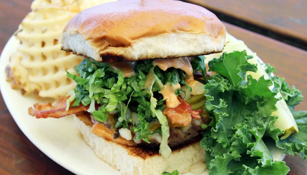 Hamburger with bacon, cheese, lettuce, sauce; waffle fries and salad.