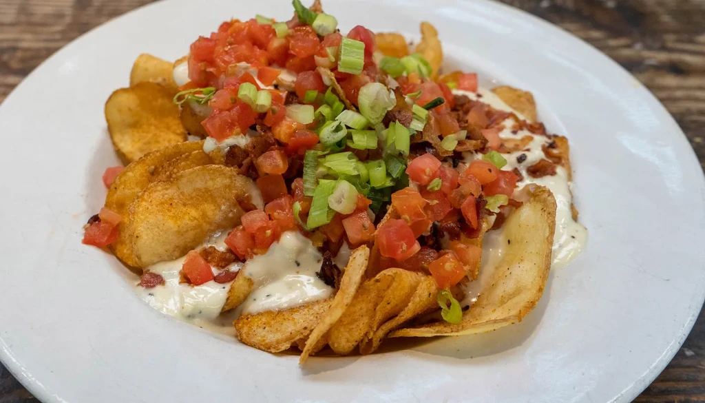 Close-up of loaded potato wedges with sauce, tomatoes, bacon, and scallions.