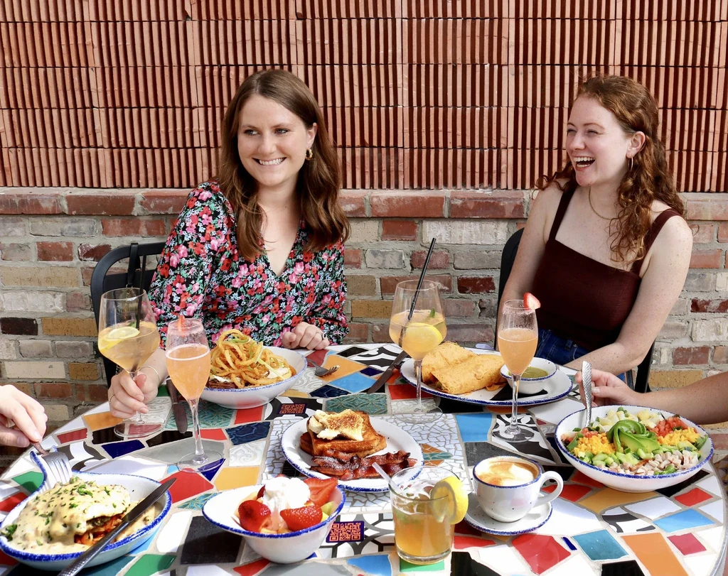 Vibrant outdoor dining with two smiling women, food, and drinks.