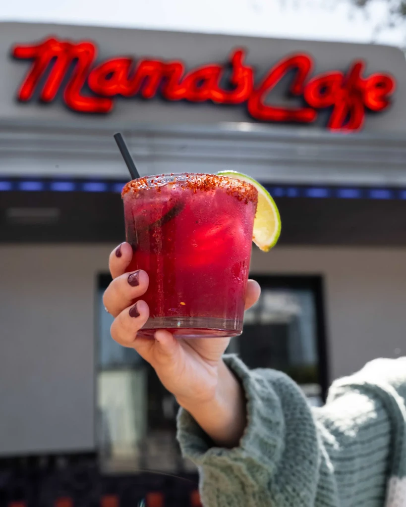 Hand holds a spiced reddish-purple drink with lime outside Mama's Cafe.