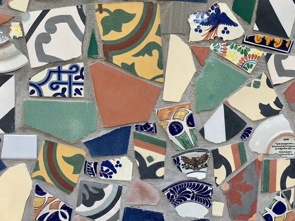 Colorful Talavera-style mosaic of ceramic shards with floral, bird patterns, and text.