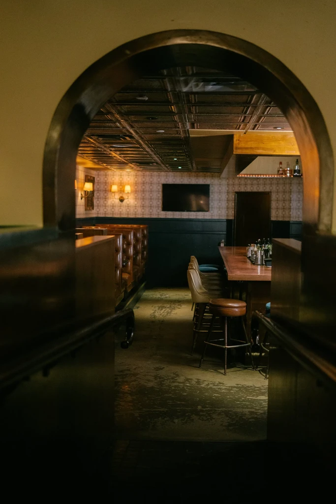 Restaurant bar interior seen through archway, with booths and wooden bar.