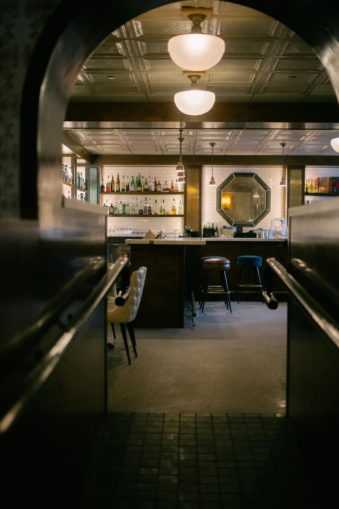 Elegant bar interior with liquor bottles, octagonal mirror, and bar stools.