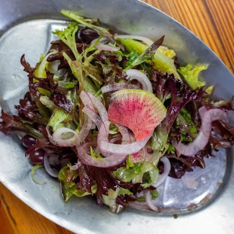 Salad with greens, watermelon radish, and onion in metallic trough.