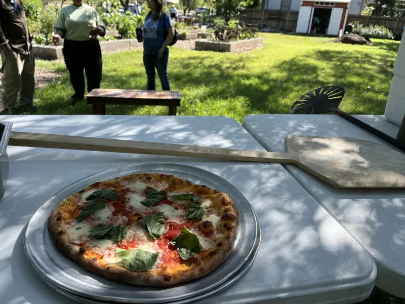 Freshly baked Margherita pizza on outdoor table with pizza peels.