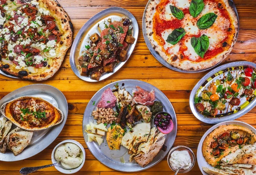 Overhead view of two pizzas and several platters of abundant food.