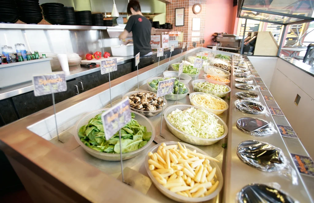 Well-lit self-serve bar overflowing with fresh, labeled salad ingredients.
