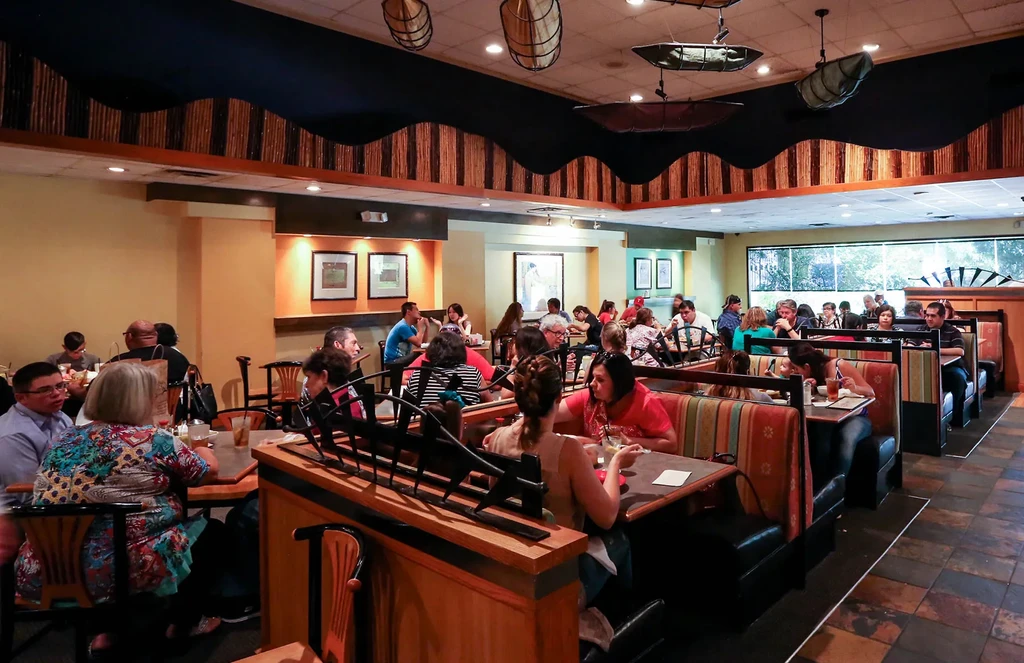Lively restaurant interior with patrons, suspended boats, and colorful decor.