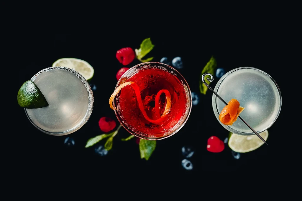Three distinct cocktails garnished with fruit and mint on black.