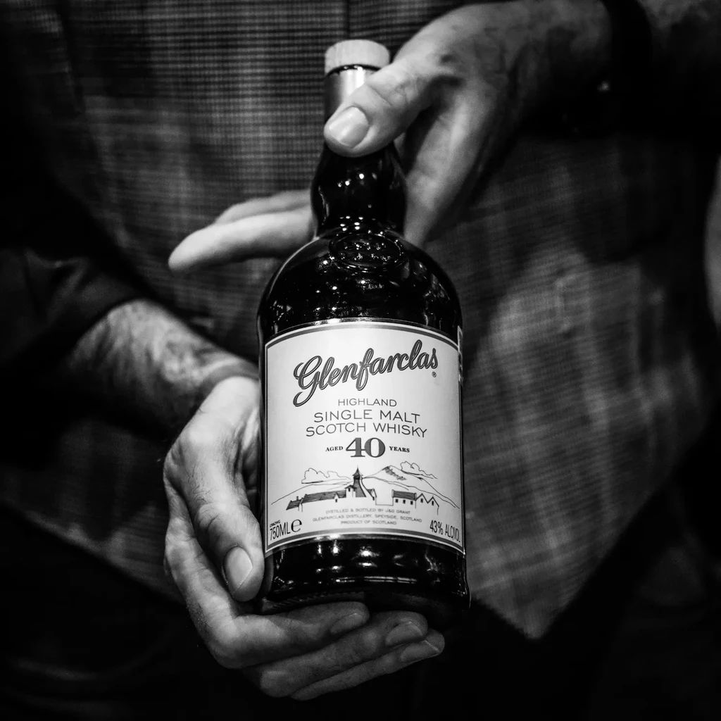 Glenfarclas 40-year whisky bottle held by hands, black and white photo.