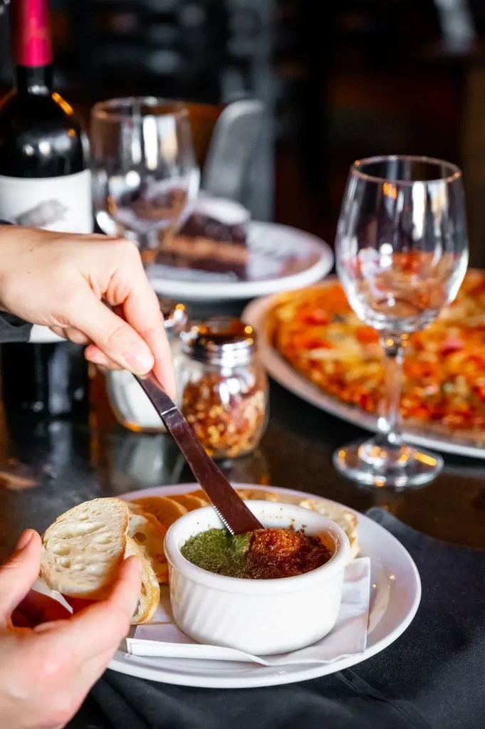 Overhead: hands scooping dip onto bread, pizza, red wine, and cake.