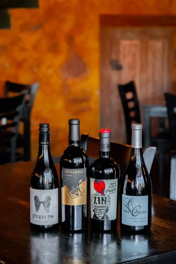 Four dark glass wine bottles on a table, blurred restaurant background.