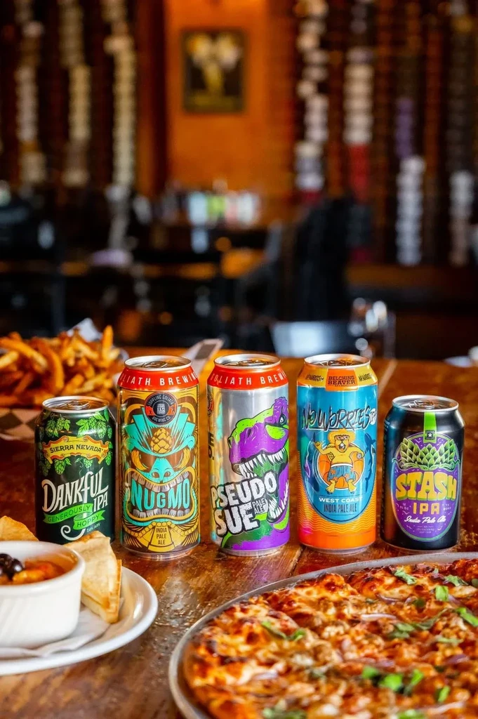 Colorful beer cans, pizza, fries, and dip on a wooden table.