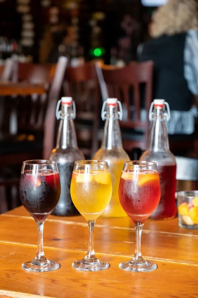 Three chilled colorful fruit drinks and bottles on a wooden table.