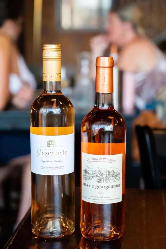 Two rosé wine bottles on a dark table in a blurred bar setting.