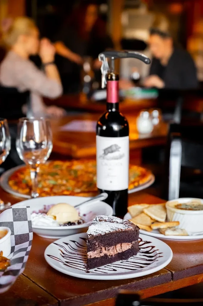 Chocolate cake, ice cream, pizza, and wine on a restaurant table.