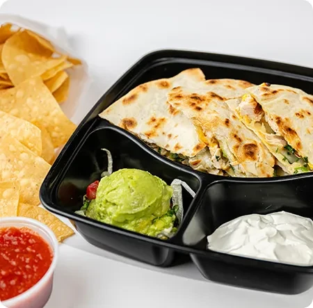 Black takeout container holds quesadillas, guacamole, sour cream, chips, and salsa.
