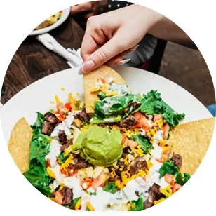 Hand dipping a chip into a taco salad with meat and veggies.